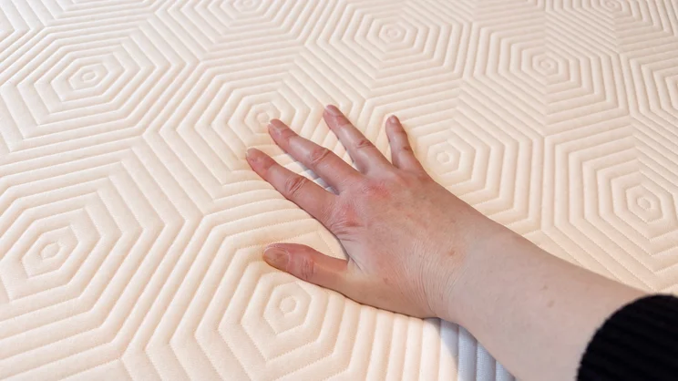 The surface of the TEMPUR EASE mattress. A hand is pressing down on it