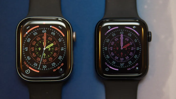 The Apple Watch SE 3 (right) lying flat on a blue and white mat next to an Apple Watch Series 11