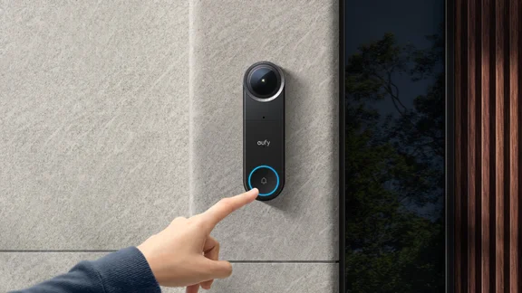 The Eufy Video Doorbell S4 mounted on a white rendered wall next to a dark wood door, modern architecture