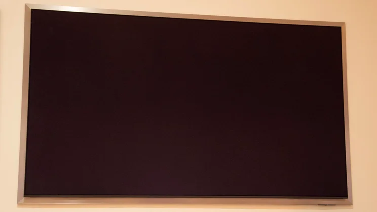 The Samsung S95H QD-OLED TV mounted on a wall with no picture displayed on screen