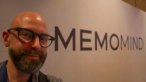 Tech Editor Andy White wearing the XGIMI Memo One smart glasses in front of a MemoMind sign in Las Vegas