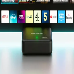 The Manhattan Aero 4K TV Streamer in front of a TV displaying a row of apps, including Freely