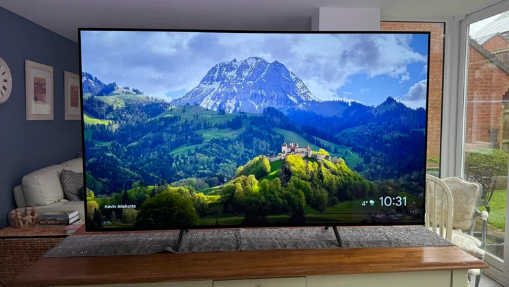 Front view of the Philips OLED810 TV displaying a mountain scene while on a table in an open-plan kitchen