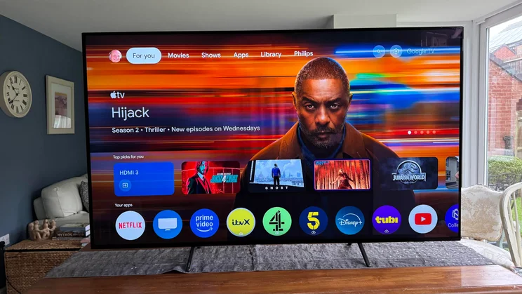 Front view of the Philips OLED810 TV displaying the Google TV homepage while on a table in an open-plan kitchen
