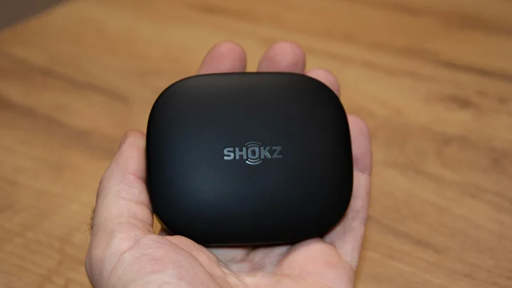 The Shokz OpenFit Pro charging case being held in the palm of a hand