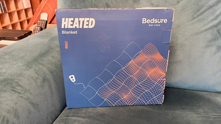 The Bedsure Heated Blanket Electric Throw in its box, on a sofa