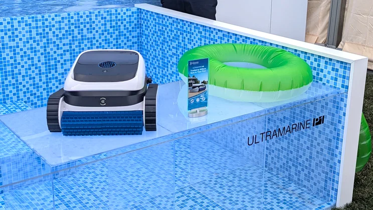The Ecovacs Ultramaine P1 swimming pool cleaner on display next to a model swimming pool