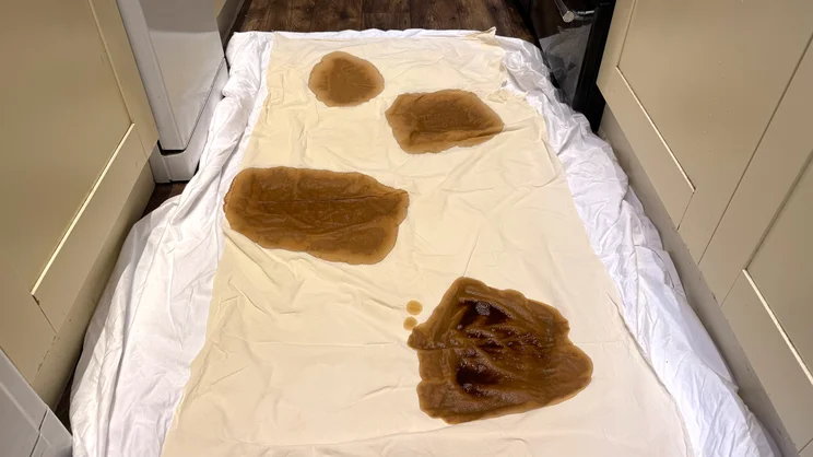 A series of coffee stains on a sheet, placed on the Panda Bamboo mattress protector, on a kitchen floor