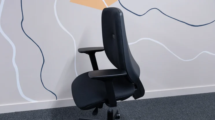 A side view of the Posturite Homeworker Plus office chair against an office wall, the backrest leaning forwards