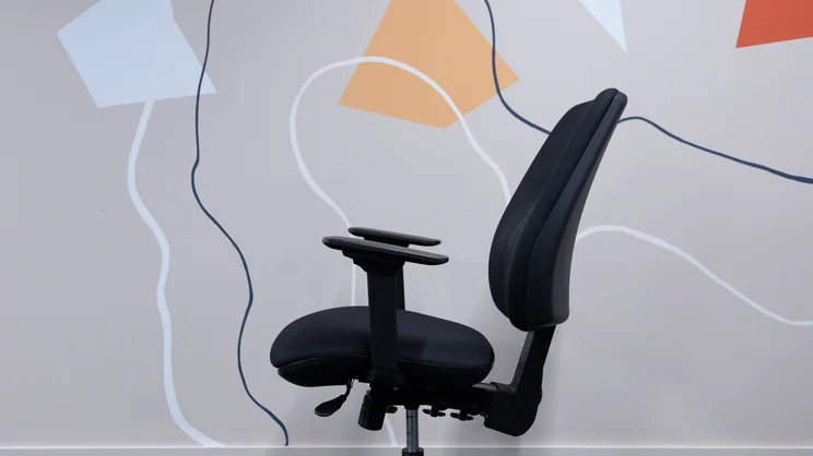 The Posturite Homeworker Plus office chair viewed from the side, in an office against a wall. The backrest is reclined slightly