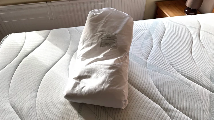 The Scooms 100% Pure Cotton mattress protector in its storage bag, on top of a mattress