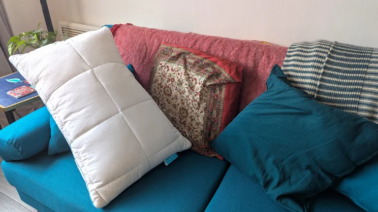 The Simba Aerodown pillow propped up on a blue sofa, among cushions