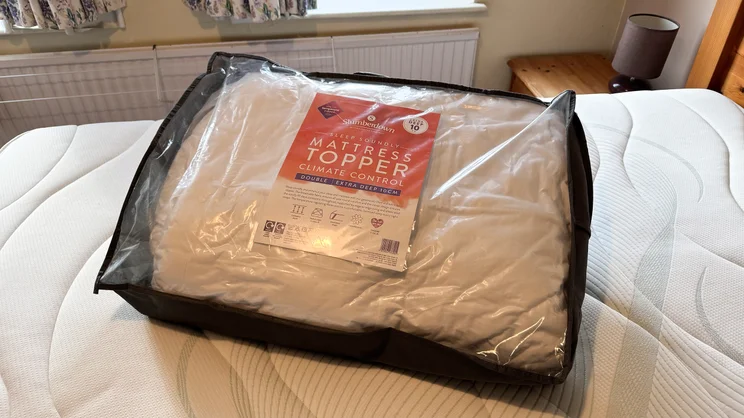 The The Slumberdown Sleep Soundly Extra Deep Climate Control mattress topper in its bag, on top of a mattress