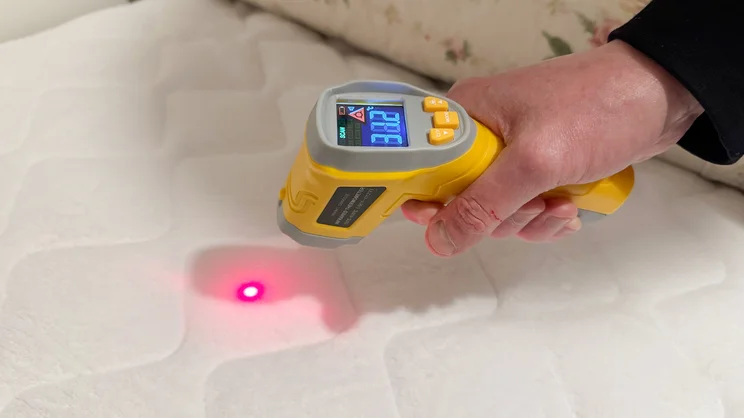 An infrared thermometer gun being used to measure the temperature of the Slumberdown Wonderfully Warm Electric Blanket's surface