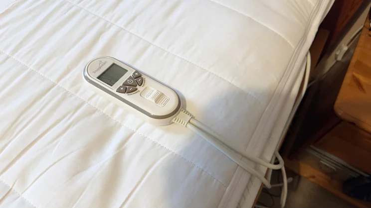 The Snuggledown Intelligent Warmth electric blanket on a mattress, with its remote control placed on top