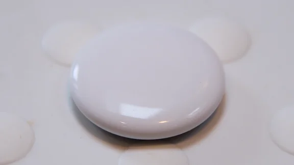 The Apple AirTag (2nd gen) pictured on a white rubber surface