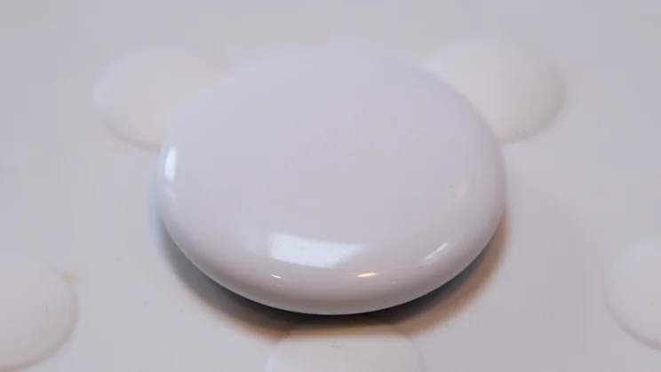 The Apple AirTag (2nd gen) pictured on a white rubber surface