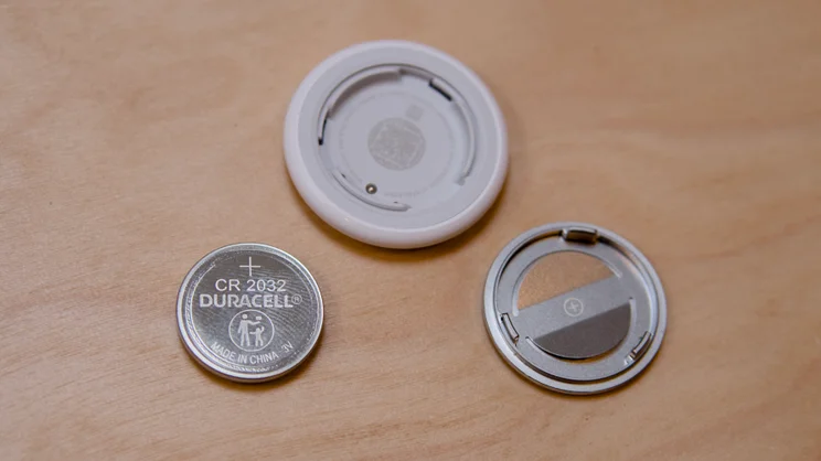 The Apple AirTag (2nd gen) pictured with the rear removed and the battery pulled out of it