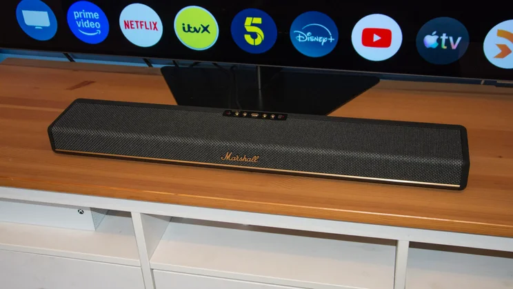 The Marshall Heston 60 soundbar on a wooden cabinet underneath a television