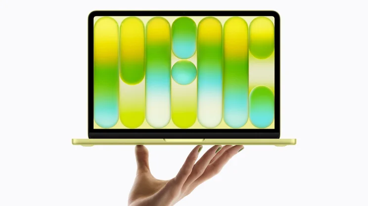 A render of the Apple MacBook Neo in citrus, open, being propped up on a hand