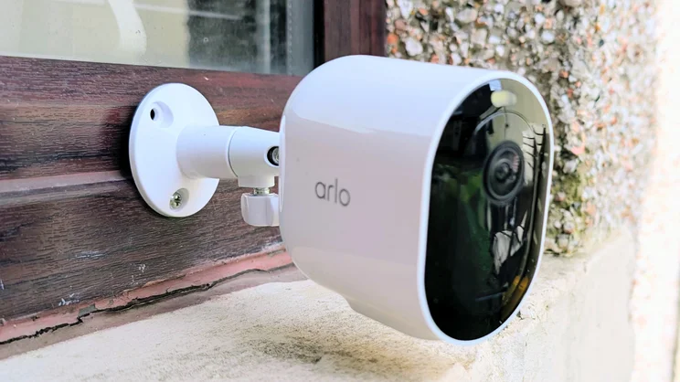 Arlo Pro 6, pictured from the left side, attached to a wood window frame
