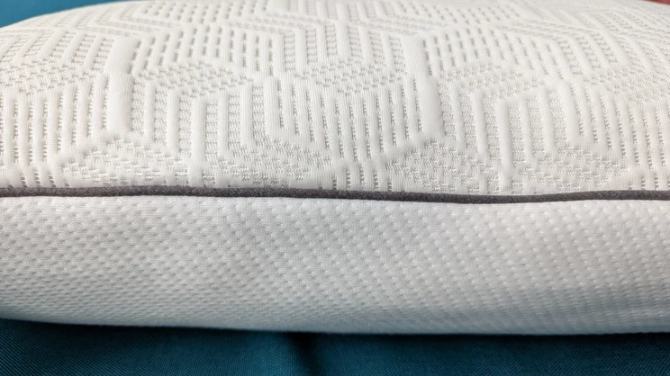 A closeup side view of the Dreams Hyde and Sleep Dual Comfort Ice pillow, showing its contrasting surfaces and piped edging
