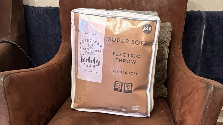 The Dunelm Teddy Electric Throw in its case, on a brown chair