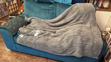 The Dunelm Teddy Electric Throw draped over a blue sofa in a living room