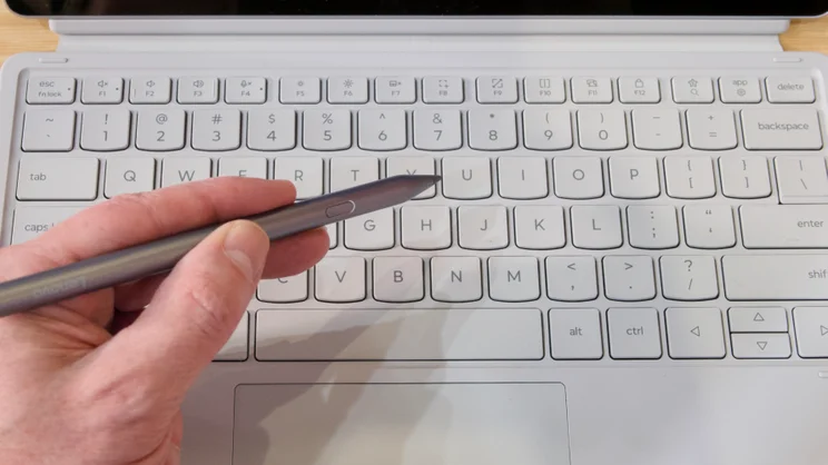 A hand, grasping the Lenovo Tab Pen Plus, with the Lenovo Idea Tab Pro Gen 2's keyboard in the background