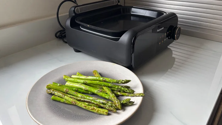 A plate of cooked asparagus, in front of the Panasonic 6-in-1 Table-top Multi Cooker, on a kitchen surface