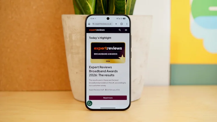 Poco X8 Pro leaning against a plant pot, displaying Expert Reviews homepage