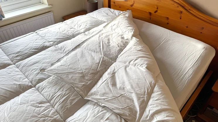The Soak & Sleep Soft as Down duvet on a mattress, with one corner folded back