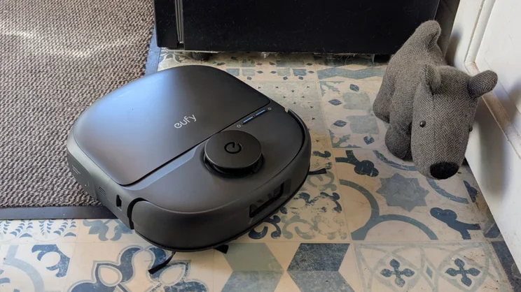 The Eufy Omni C28 pictured cleaning some blue linoleum with a stuffed dog next to it