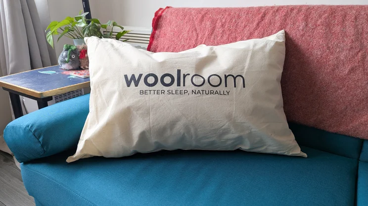 The Woolroom Deluxe Washable Wool Pillow in its canvas bag, on a blue sofa