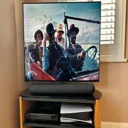 The Bluesound Pulse Cinema Mini soundbar on a TV stand in front of a Philips television
