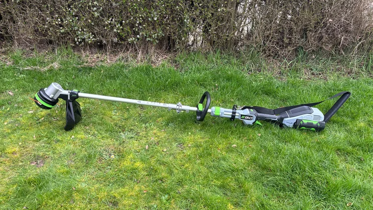 The Ego ST1511E-T grass trimmer laid flat on a lawn, in front of a hedge