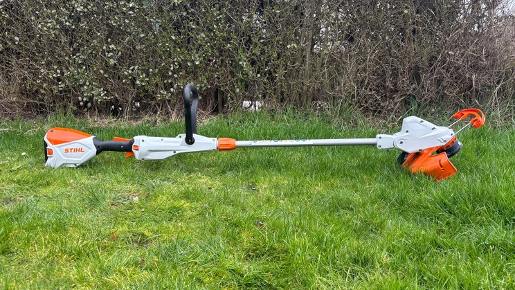 The Stihl FSA 50 grass trimmer lying down on a lawn, in front of a hedge