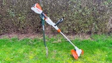 The Stihl FSA 50 grass trimmer propped upright on a spade in a garden, in front of a hedge