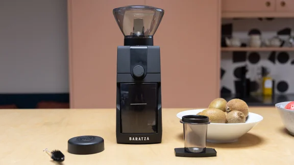 The Baratza Encore ESP Pro coffee grinder on a kitchen surface, alongside its accessories and a bowl of kiwis