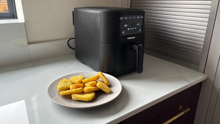 A plate of cooked hash browns in front of the Cuisinart Compact Max Air Fryer, on a kitchen worktop