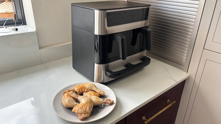 A plate of cooked chicken legs in front of the Cuisinart Tri Zone 13.6l Air Fryer & Oven, on a kitchen worktop