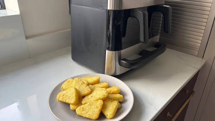 A plate of cooked hash browns in front of the Cuisinart Tri Zone 13.6l Air Fryer & Oven, on a kitchen worktop
