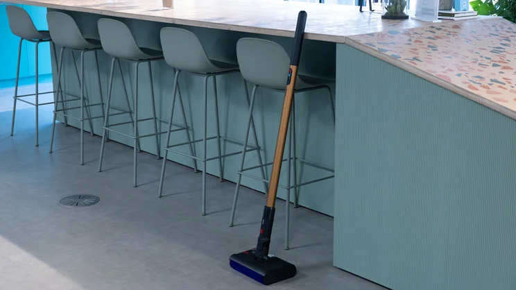 The Dyson PencilWash hard floor cleaner leaning against a tabletop in an office