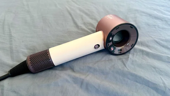 The Dyson Supersonic Travel hair dryer lying on a blue bedsheet