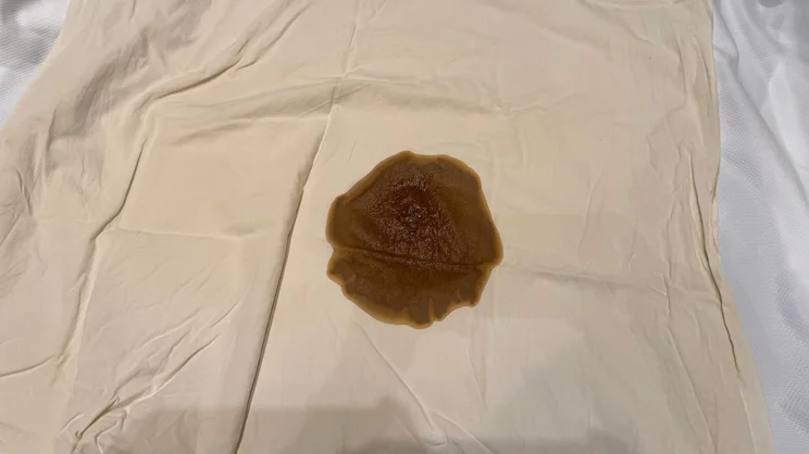 Spilled coffee on top of a beige sheet, underneath which is the Emma Mattress Protector