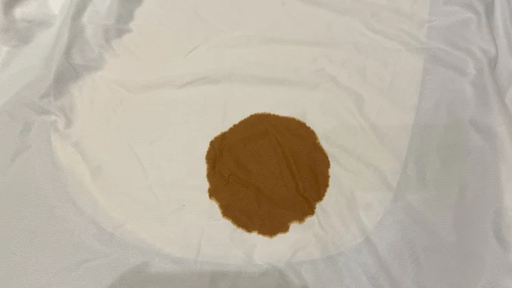 Spilled coffee on top of a beige sheet, underneath which is the Emma Mattress Protector