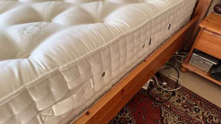 The side of the Hypnos Inspired By Nature 05 mattress, on a wooden bed frame in a bedroom