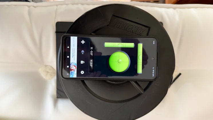 A bird's eye view of the surface of the Hypnos Inspired By Nature 05 mattress. A stack of weights has been placed on top, with a smartphone app measuring tilt