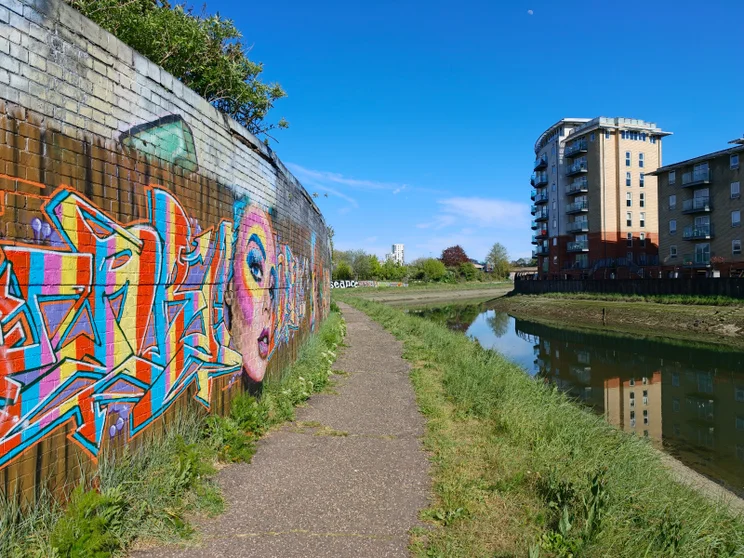 A path alongside a river with a graffitied wall