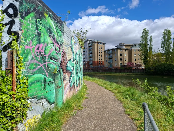 A path by a river with a graffitied wall